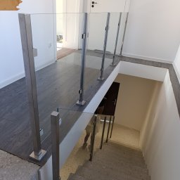 MS-PRO Marek Szczepanek - Szklana balustrada z metalowymi słupkami zabezpieczająca schody w nowoczesnym wnętrzu, widok z góry na betonowe schody.