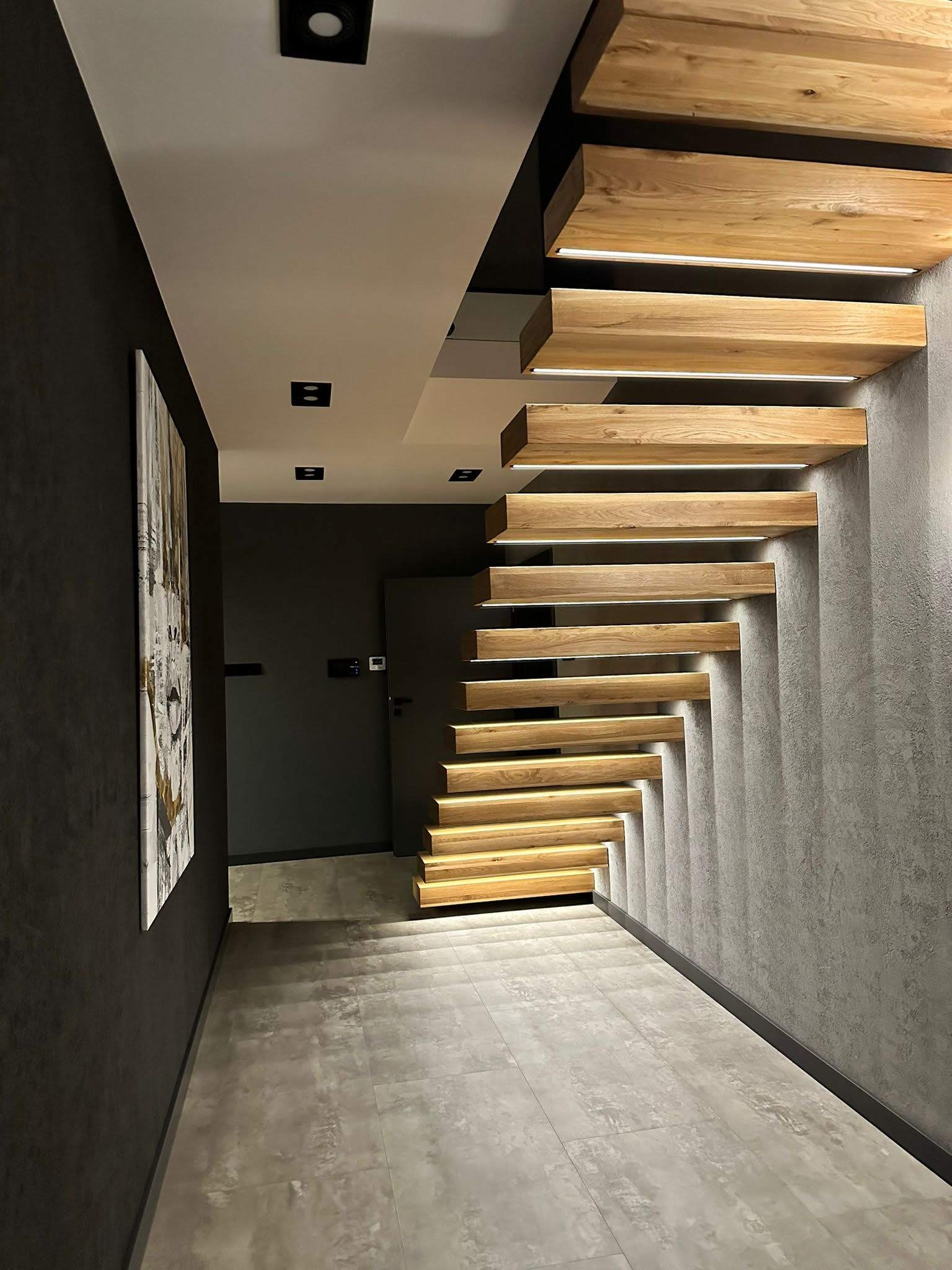Nowoczesne schody z drewnianymi stopniami podświetlonymi od spodu, w minimalistycznym wnętrzu z szarą ścianą i podłogą.