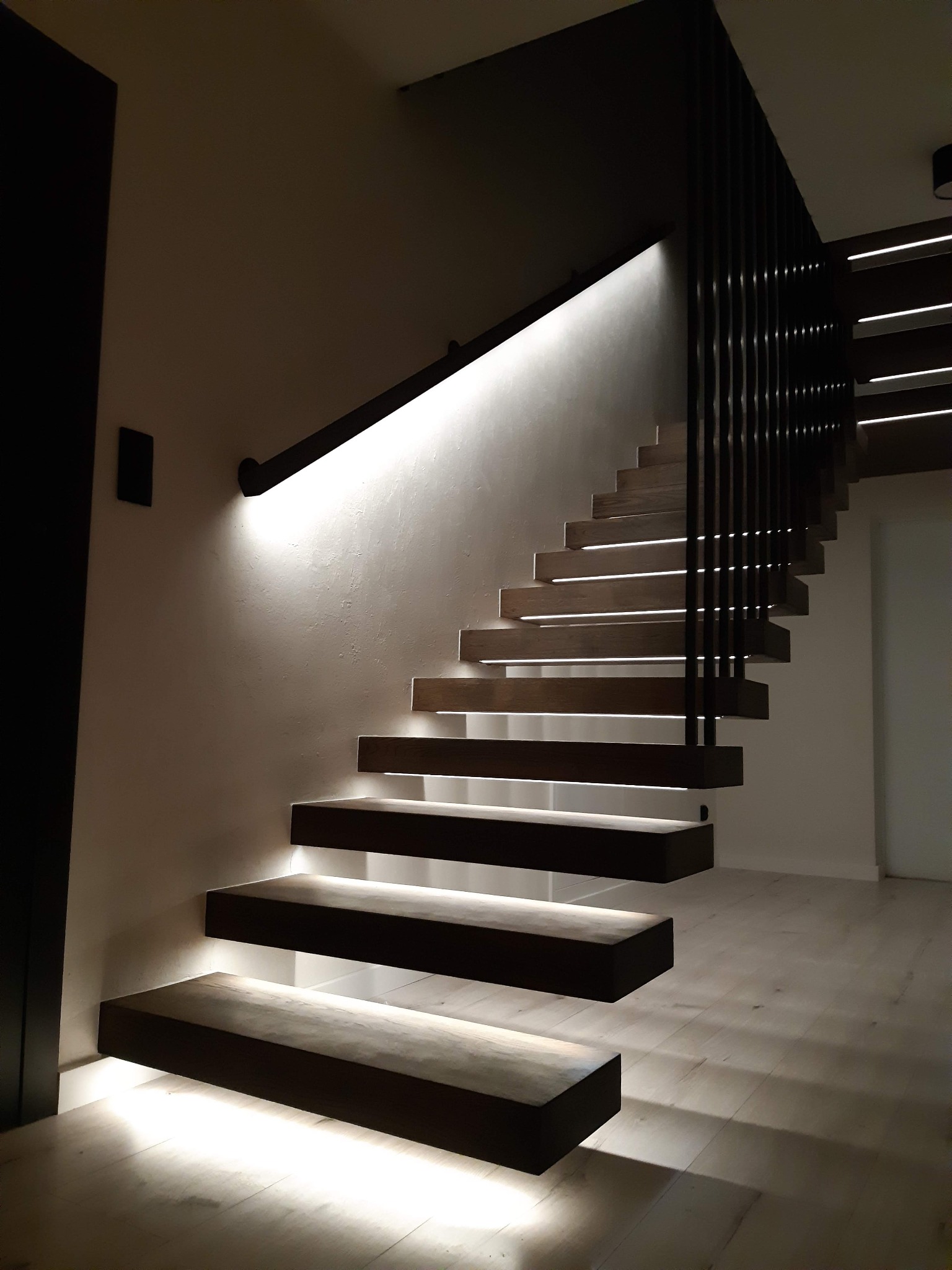 Nowoczesne, podświetlane schody metalowe z drewnianymi stopniami i czarną balustradą w Łodzi. Minimalistyczny design z subtelnym oświetleniem LED podkreślającym konstrukcję.