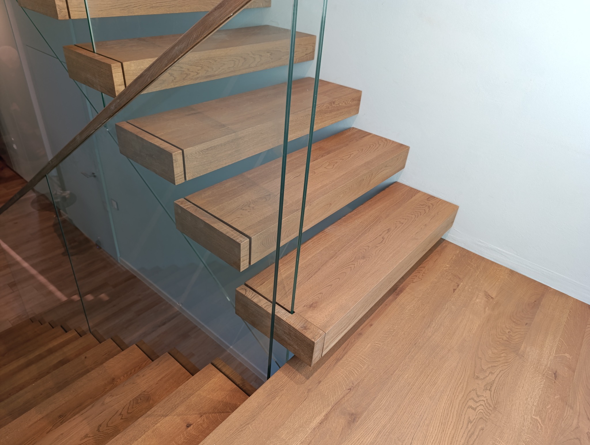 Drewniane schody wiszące z balustradą ze szkła hartowanego, widok z góry, naturalne oświetlenie podkreśla strukturę drewna.