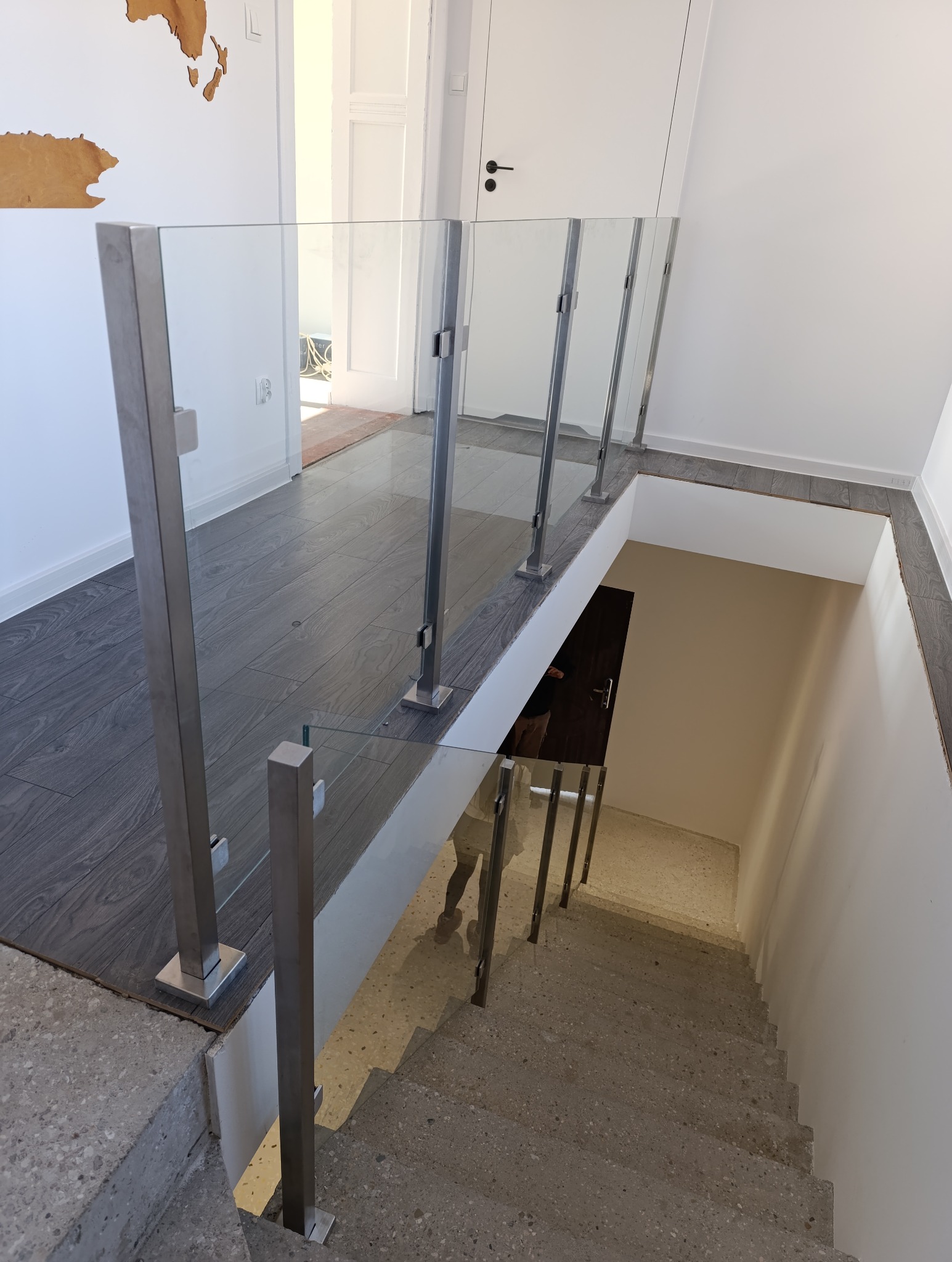 Szklana balustrada z metalowymi słupkami zabezpieczająca schody w nowoczesnym wnętrzu, widok z góry na betonowe schody.