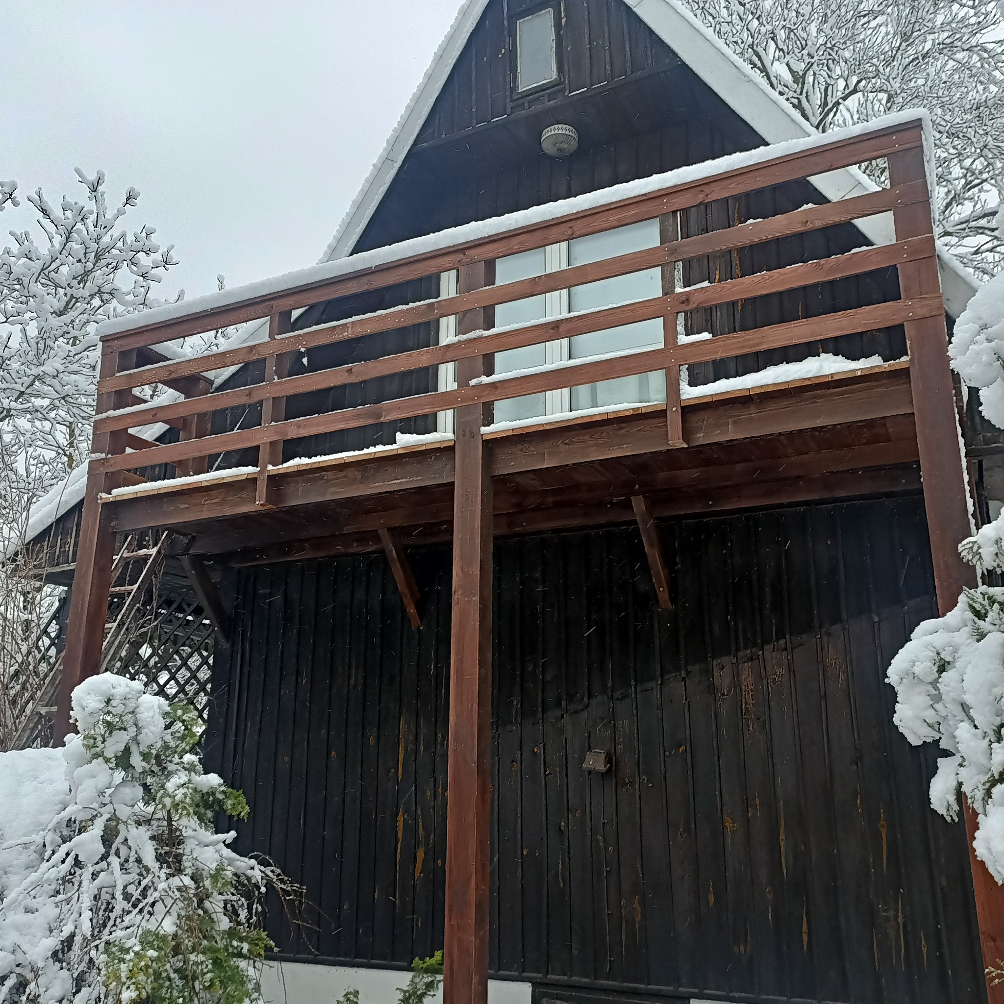 Drewniany dom z balkonem i schodami zewnętrznymi, pokryty śniegiem podczas zimy.