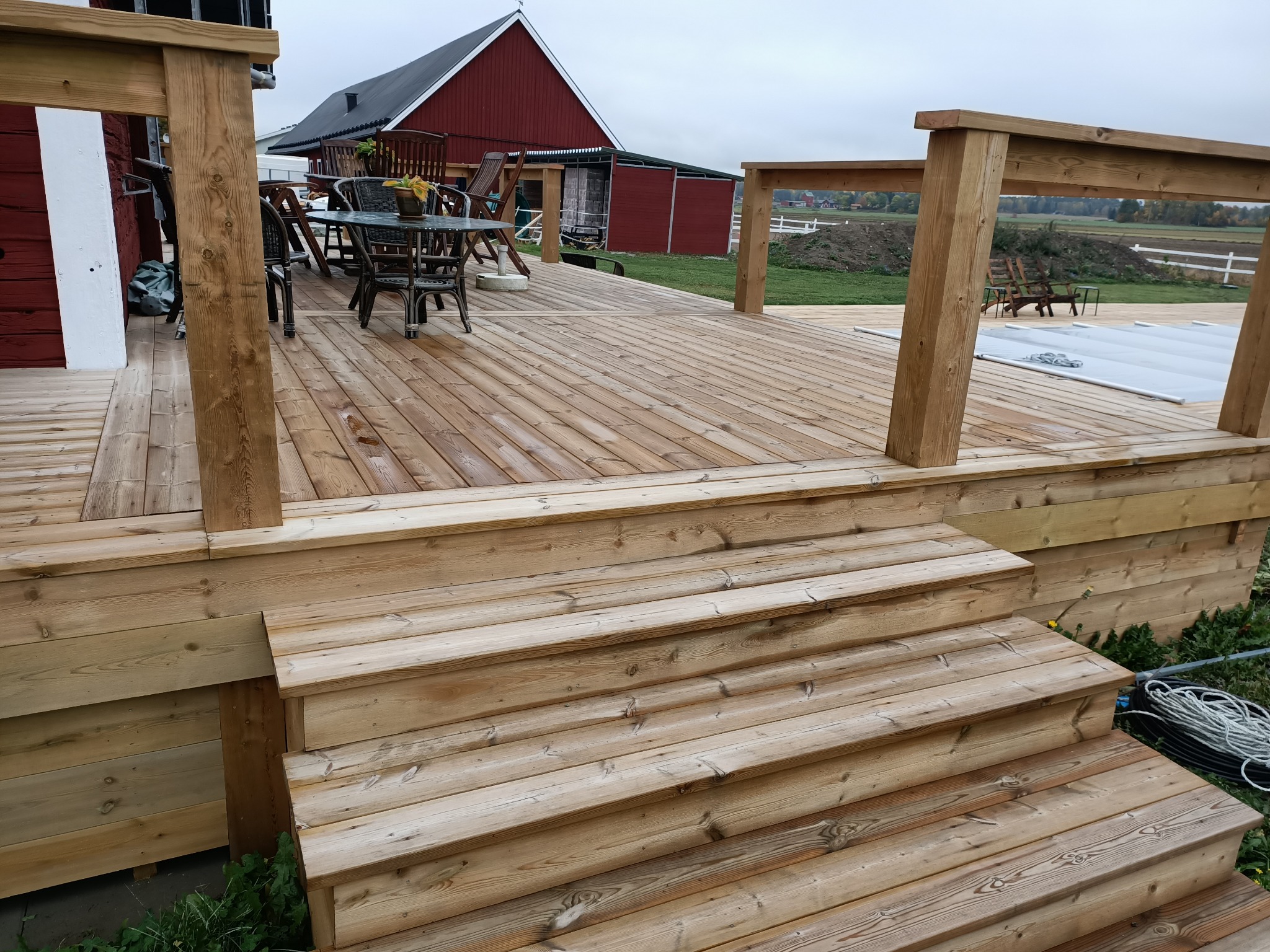 Nowo wybudowany drewniany taras z schodami w Olsztynie, widok na ogród i budynek gospodarczy w tle.