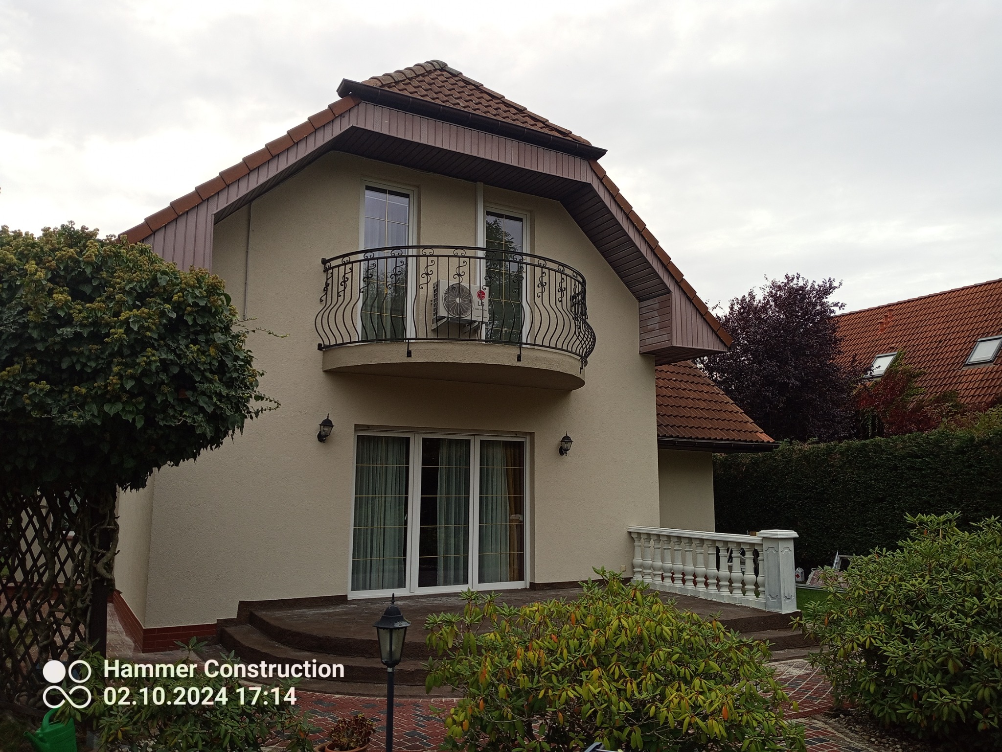 Elewacja domu z balkonem w Trzcińsko-Zdrój. Kremowa fasada, ozdobny balkon z kutą balustradą. Widoczne detale wykończenia i otoczenie budynku.
