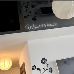 Wnętrze z białymi ścianami, czarnymi naklejkami z motywem kwiatowym, napisem 'Wizard's house' i dwoma papierowymi lampami kulami.