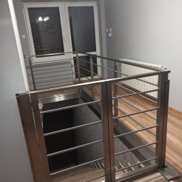 Metal Project - Nowoczesna, nierdzewna balustrada schodowa z poziomymi prętami, widok z góry na schody wykończone szarą płytką, z drewnopodobną podłogą na górnym poziomie i oknem w tle.