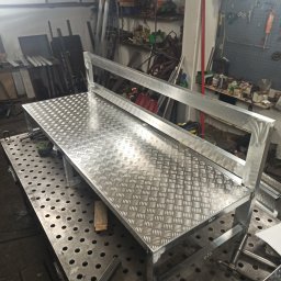 Metal Project - Metalowa konstrukcja z blachy ryflowanej na stole spawalniczym, widoczne narzędzia i elementy warsztatu w tle.