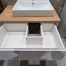 Tomasz Kuczynski - Nowoczesna łazienka z białą umywalką nablatową na blacie z drewna oraz szafką z szufladą z połyskiem, widoczny fragment toalety wiszącej.