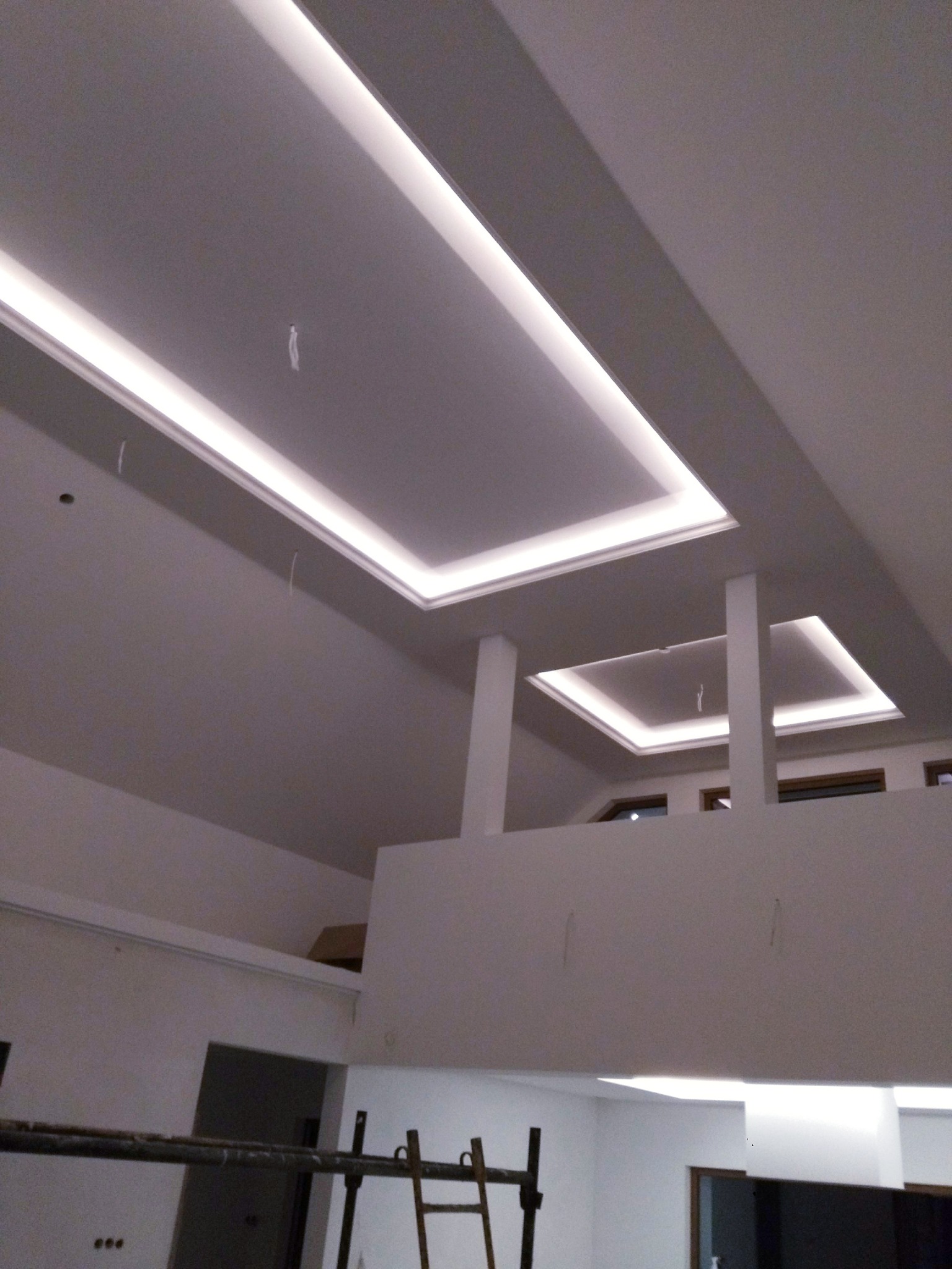 Nowoczesne oświetlenie sufitowe LED w jasnym wnętrzu z antresolą, widoczne elementy rusztowania.