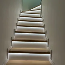 Nowoczesne schody z podświetleniem LED, drewniane stopnie z białymi listwami, oświetlenie wbudowane pod każdym stopniem, minimalistyczny design, jasne ściany.