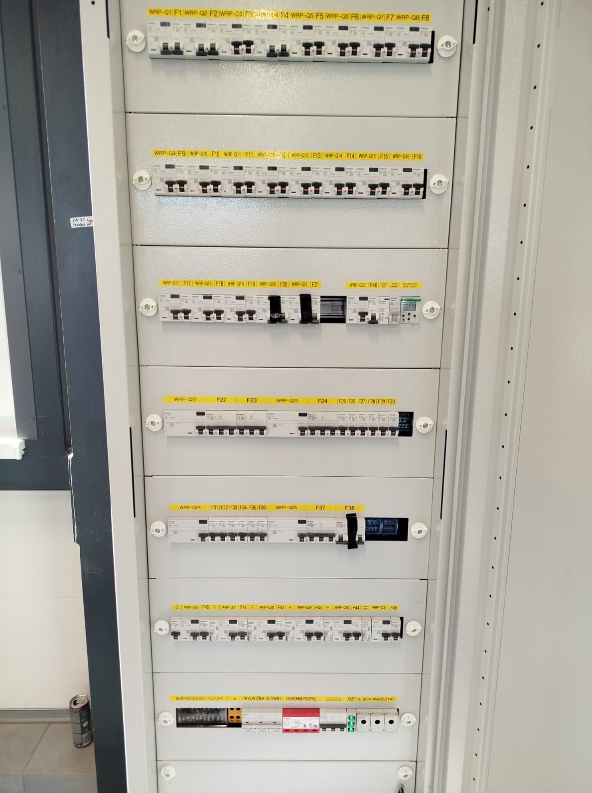 Szczegółowe ujęcie rozdzielnicy elektrycznej z licznymi bezpiecznikami i oznaczeniami, widoczne okablowanie i elementy sterujące.
