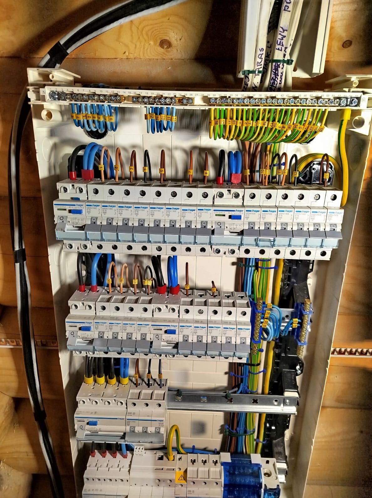 Rozdzielnica elektryczna Hager z bezpiecznikami, okablowaniem oznaczonym numerami i listwami zaciskowymi, zamontowana na drewnianej ścianie.