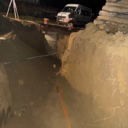 INSTAL-BUD KASZUBY SPÓŁKA Z OGRANICZONĄ ODPOWIEDZIALNOŚCIĄ - Wykop pod instalację wod-kan nocą, widoczny rów z rurą, samochód dostawczy i niwelator laserowy. Prace ziemne przy oświetleniu.