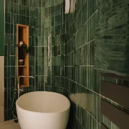 Nowoczesna łazienka z wolnostojącą, owalną wanną, zielonymi, pionowo ułożonymi płytkami z połyskiem, drewnianą półką z rośliną i grzejnikiem drabinkowym w kolorze ciemnego brązu.