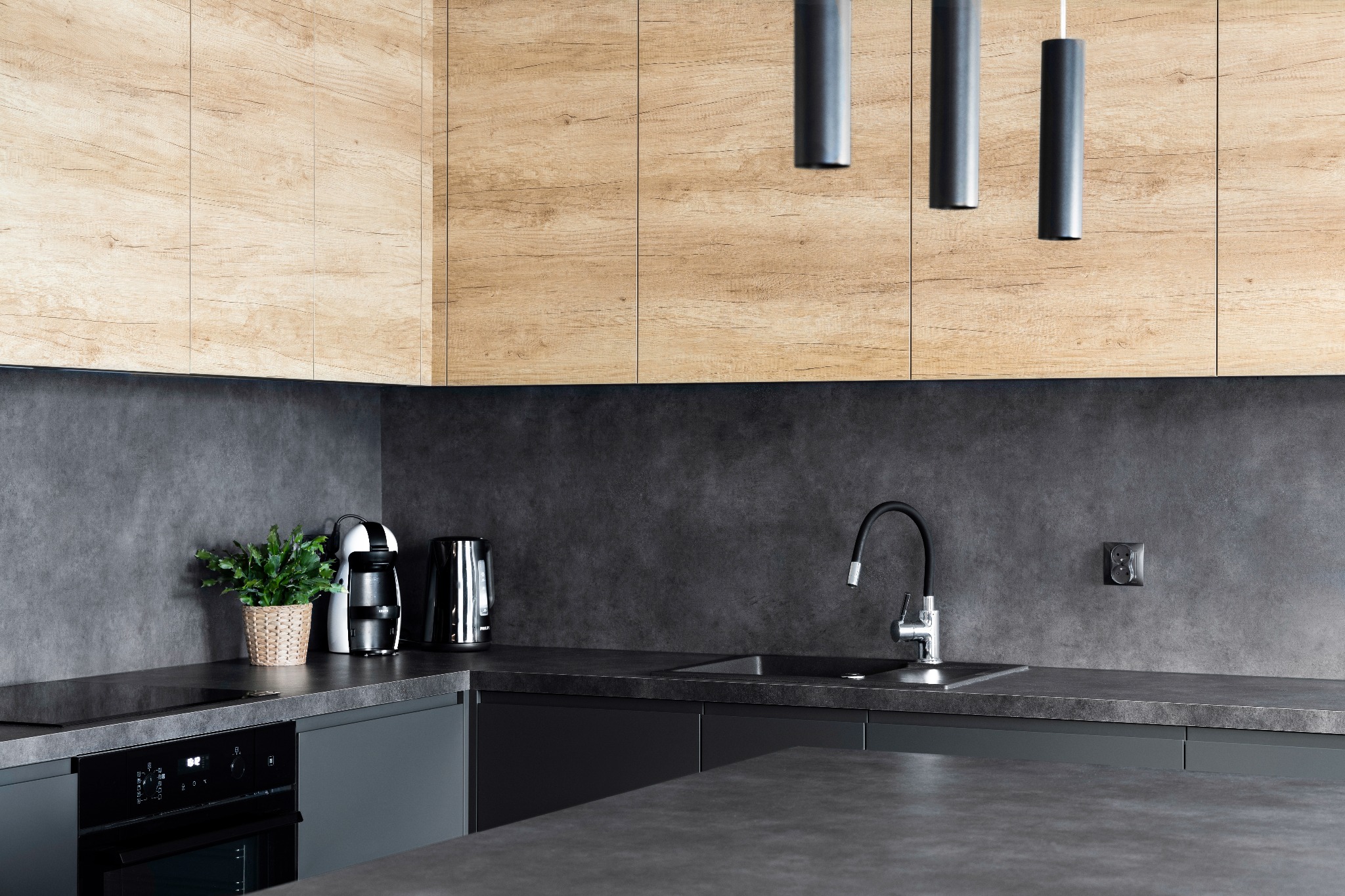Nowoczesna kuchnia we Wrocławiu z drewnianymi szafkami górnymi i grafitowymi dolnymi, czarnym blatem, minimalistyczną armaturą i oświetleniem punktowym.