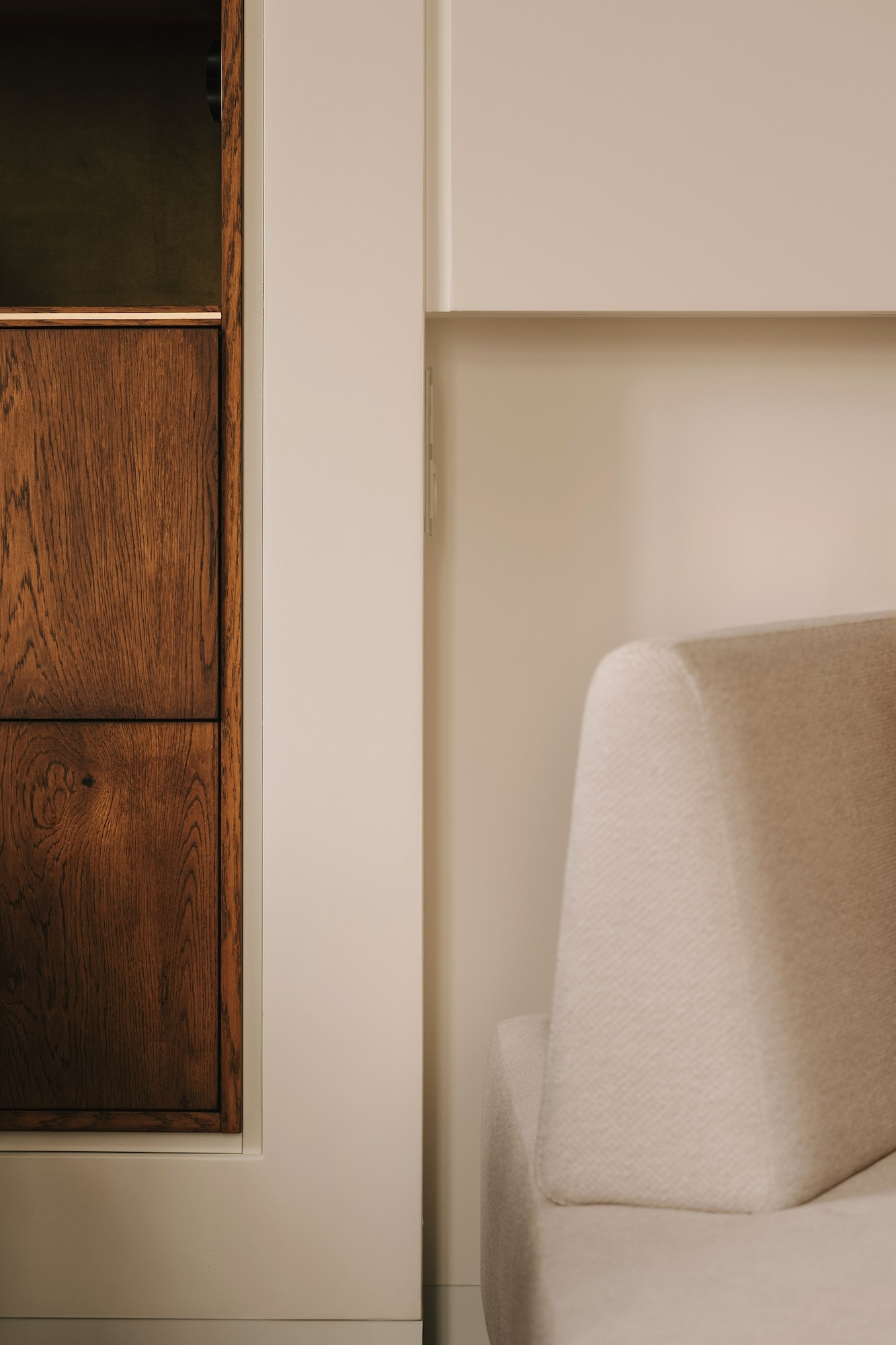 Fragment wnętrza z drewnianą szafką o widocznym usłojeniu i kremową sofą o minimalistycznym designie.