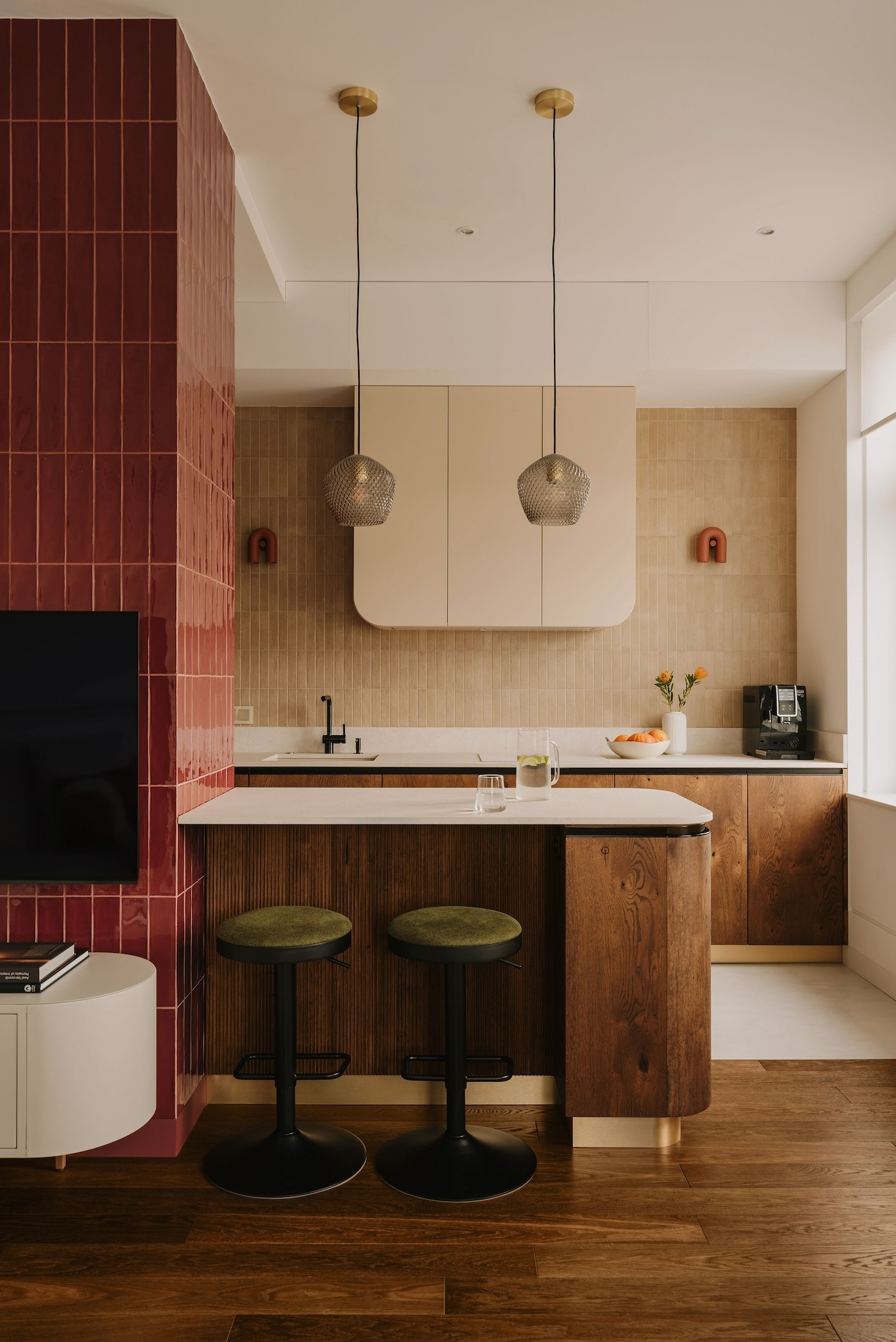 Nowoczesna kuchnia z wyspą, drewnianymi szafkami i blatem z białego marmuru, oświetlona lampami wiszącymi z metalowej siatki, z akcentami w kolorze ceglastej czerwieni na ścianie z płytek...