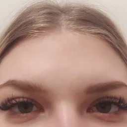 Zbliżenie na oczy kobiety z profesjonalnie przedłużonymi, gęstymi rzęsami w stylu 'kocie oko', podkreślającymi zielony kolor tęczówek.