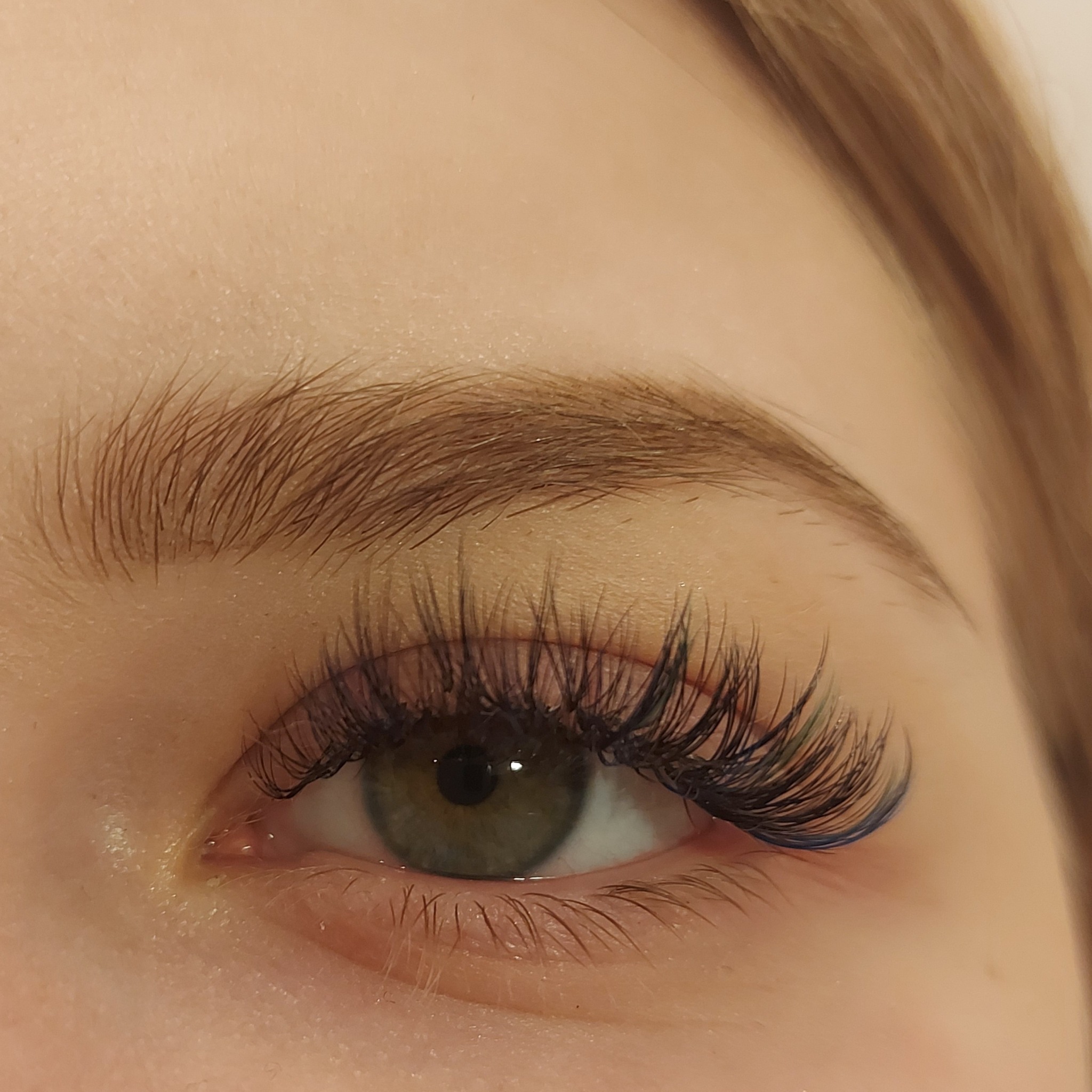Zbliżenie na oko z przedłużonymi rzęsami z subtelnym niebieskim akcentem na końcówkach, podkreślające zieloną tęczówkę.