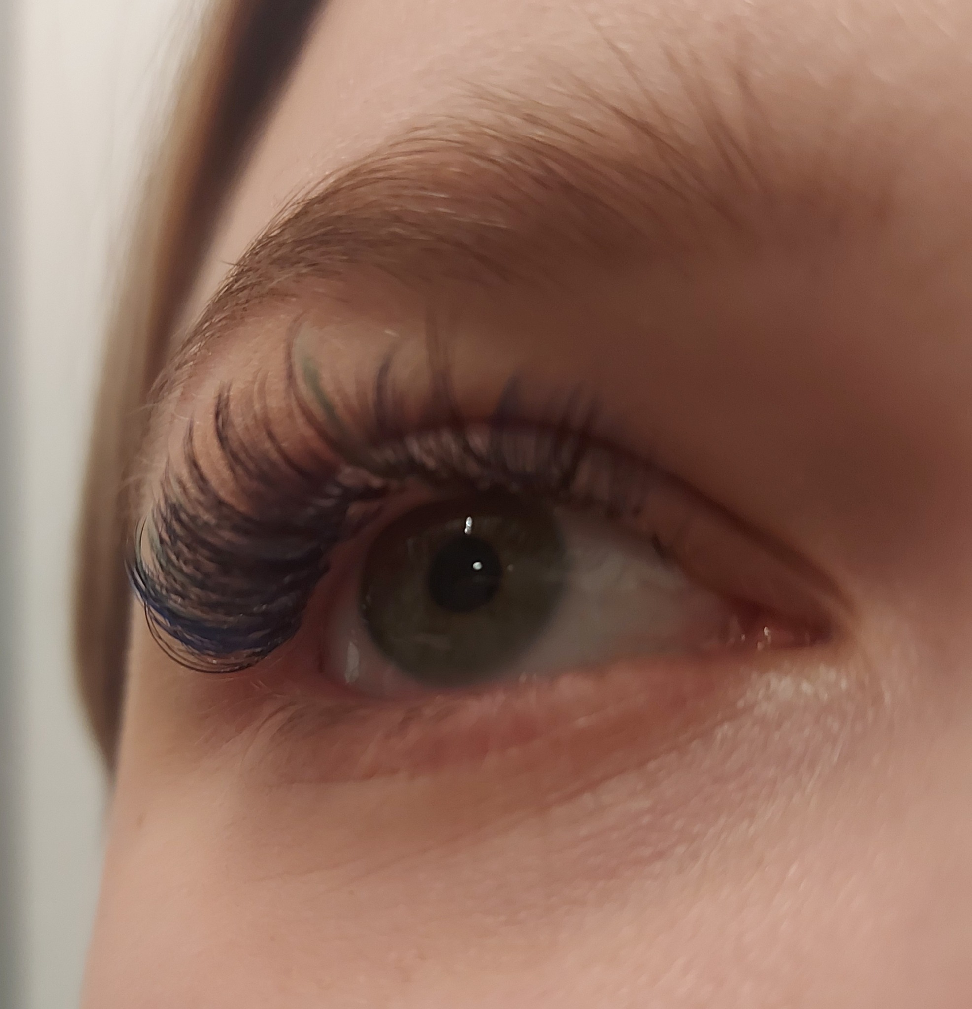 Zbliżenie na oko z przedłużonymi, ciemnymi rzęsami z niebieskimi akcentami na końcach, widoczny fragment brwi