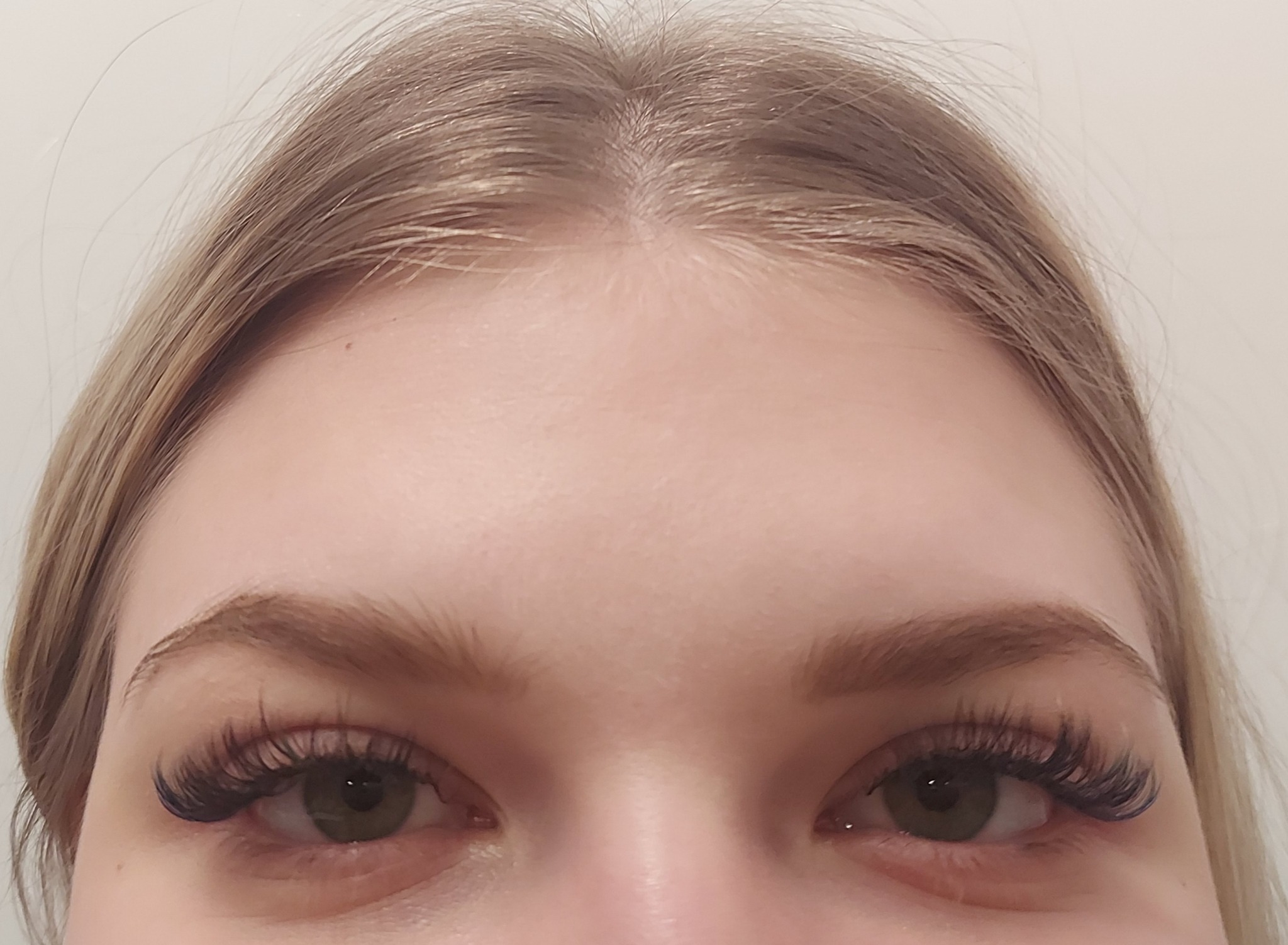 Zbliżenie na oczy kobiety z profesjonalnie przedłużonymi, gęstymi rzęsami w stylu 'kocie oko', podkreślającymi zielony kolor tęczówek.