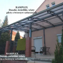 Metalowa pergola z przezroczystym zadaszeniem, wsparta na ceglanych filarach, z widocznymi elementami orynnowania i fragmentem domu z roletami.