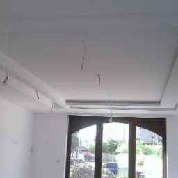 Wykończony sufit podwieszany z elementami dekoracyjnymi i wystającymi przewodami elektrycznymi, widok na okno balkonowe z widokiem na zewnątrz.