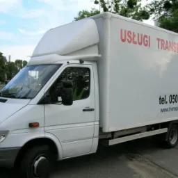 Biały samochód dostawczy z nadrukiem 'Usługi Transportowe Wrocław' oraz numerem telefonu i adresem strony internetowej, zaparkowany na ulicy.