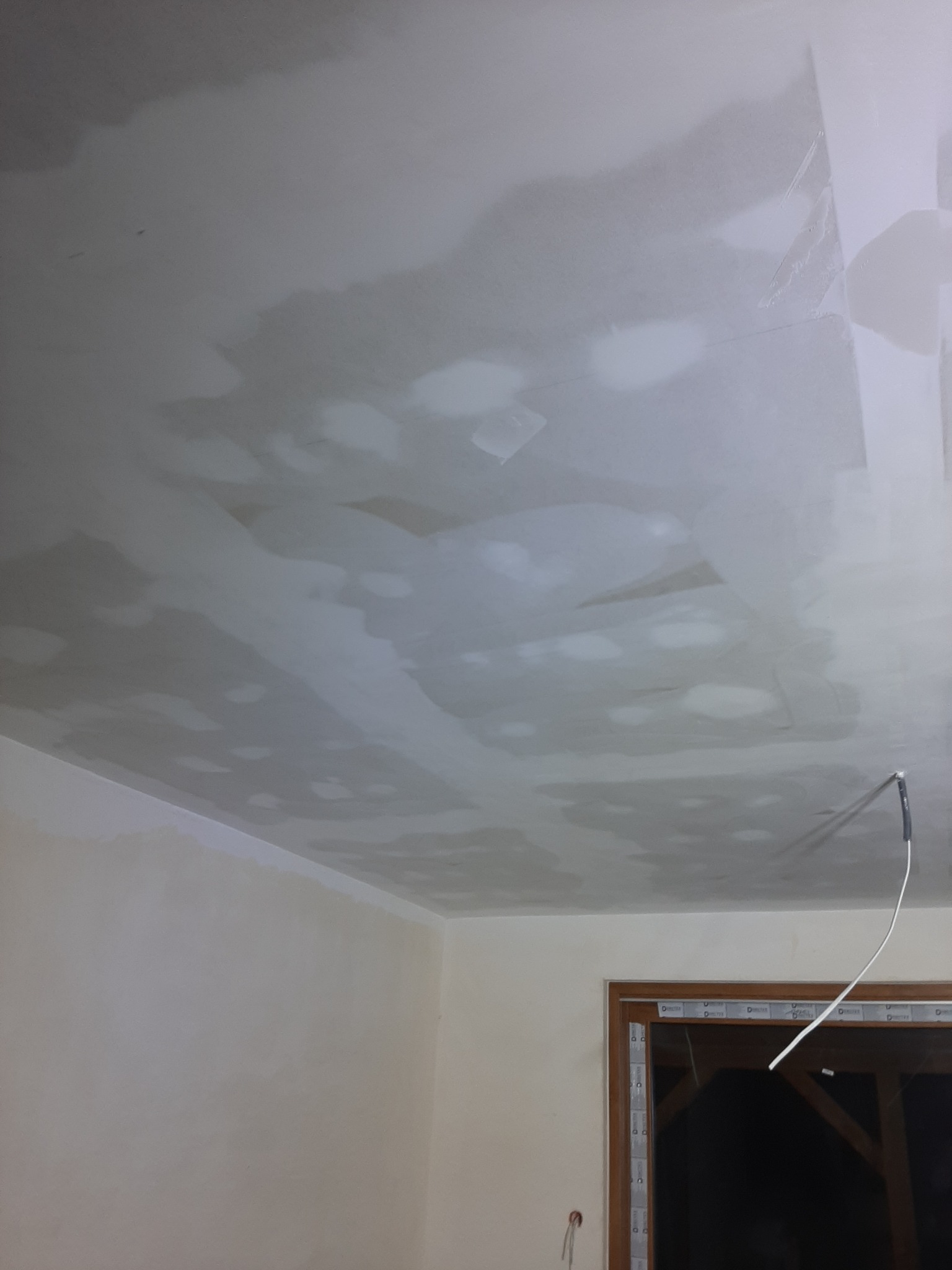 Niedokończony sufit z widocznymi łatami szpachli, przygotowany do dalszej obróbki, widoczne okno z folią ochronną.