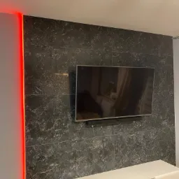 Ściana z czarnego marmuru z podświetleniem LED, na której wisi telewizor, a pod nim biała szafka RTV.