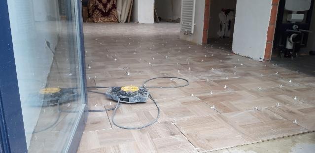 Układanie parkietu w jodełkę francuską z użyciem poziomicy laserowej, widoczne krzyżyki dystansowe, surowy stan wykończenia pomieszczenia.