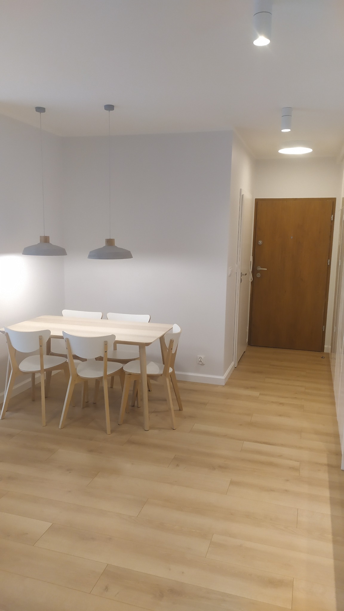 Jasne panele podłogowe ułożone w nowocześnie urządzonym pokoju w Koszalinie, z widocznym drewnianym stołem i białymi krzesłami oraz minimalistycznymi lampami wiszącymi.