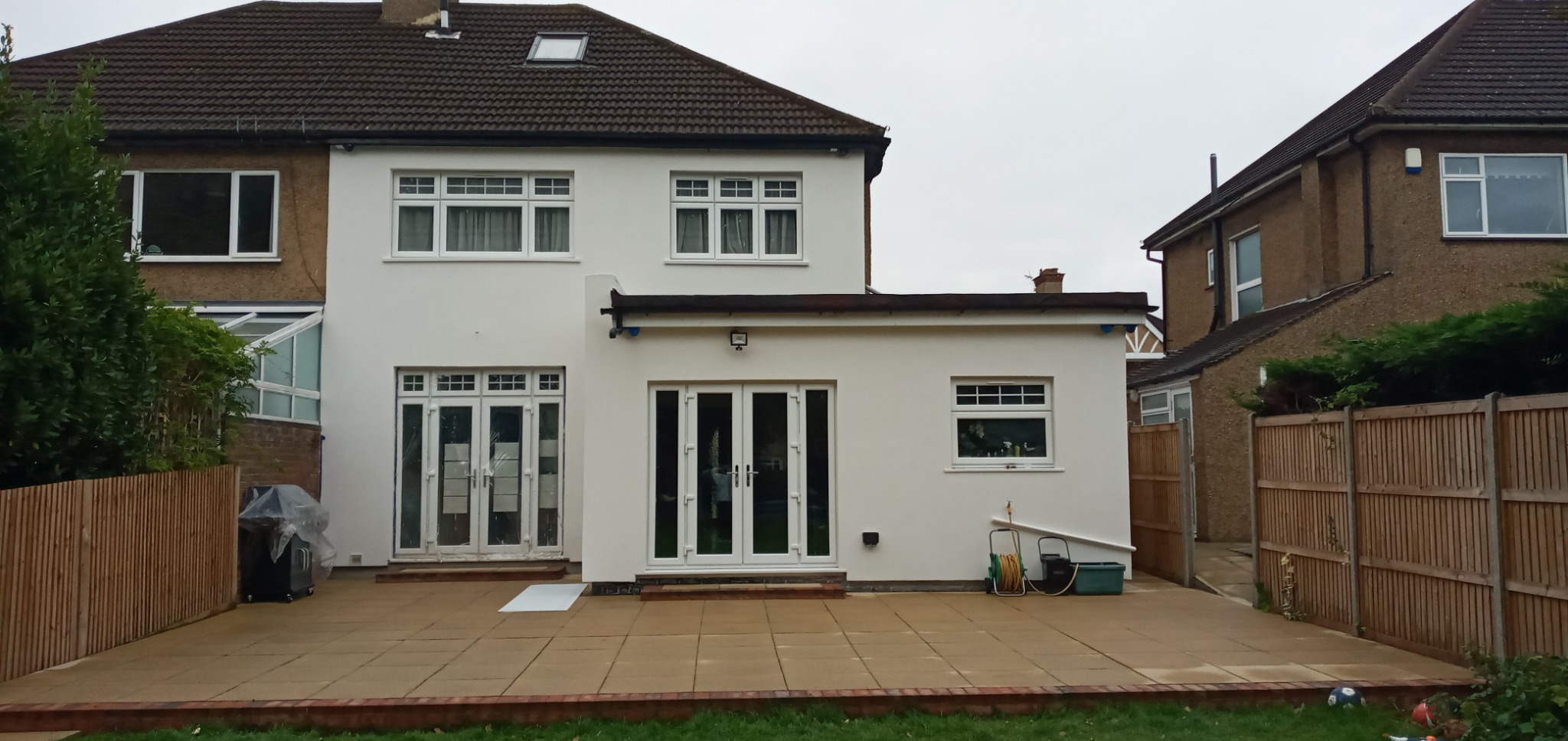 Biała elewacja domu jednorodzinnego po remoncie z widocznymi nowymi oknami i drzwiami balkonowymi, ujęcie z poziomu tarasu.