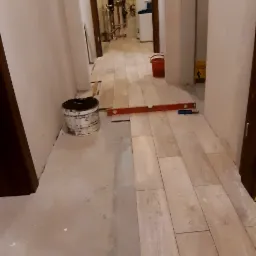 Układanie podłogi z płytek imitujących drewno w korytarzu, widoczny poziomica, wiadro z zaprawą i przygotowane podłoże