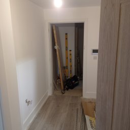 Prywatny wykonawca - Wnętrze w trakcie prac wykończeniowych: widoczne poziomy, narzędzia i otwarte puszki elektryczne na ścianie, podłoga wyłożona panelami.