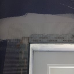 Prywatny wykonawca - Przygotowanie ściany do dalszych prac w Sanoku: siatka zbrojeniowa nałożona na ścianę nad ościeżnicą, widoczne niedoskonałości i nierówności podłoża.