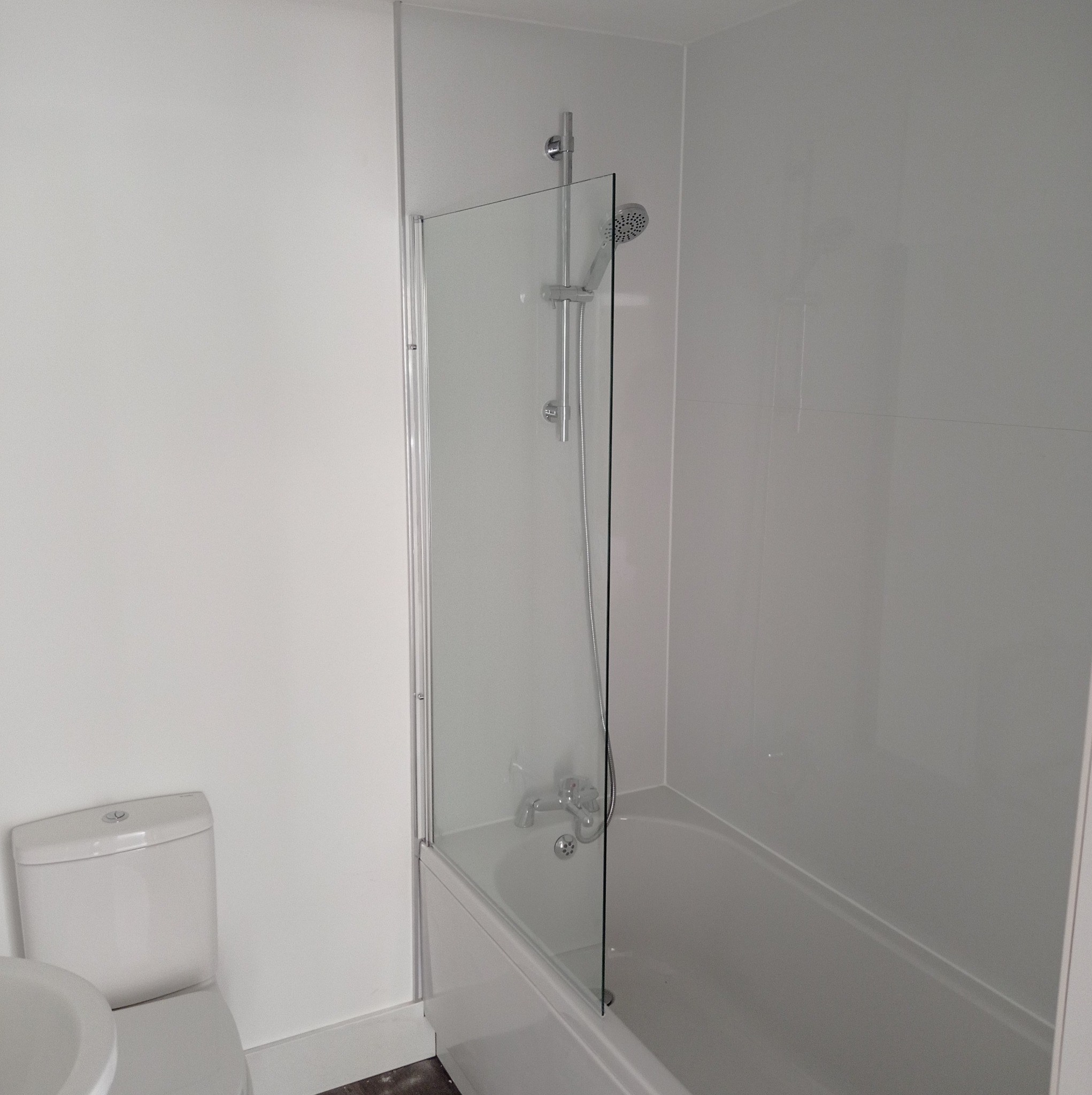 Biała łazienka po remoncie z wanną, szklanym parawanem nawannowym i toaletą.