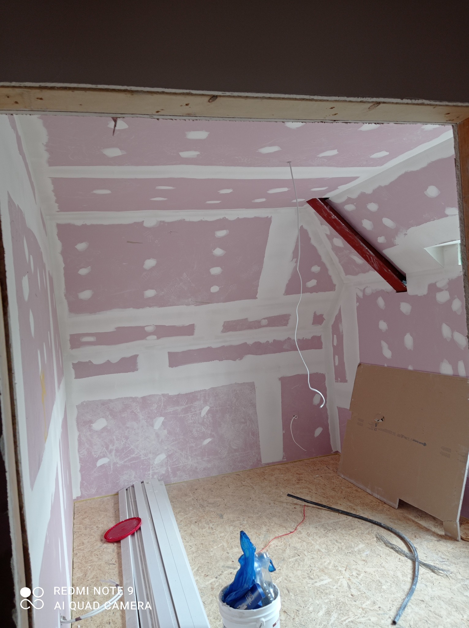 Poddasze w trakcie prac wykończeniowych: ściany pokryte płytami gipsowo-kartonowymi z widocznymi punktami mocowania, częściowo pokryte białą masą szpachlową, na podłodze płyta OSB, profile...