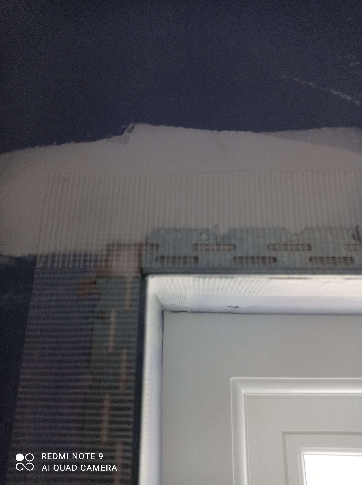 Przygotowanie ściany do dalszych prac w Sanoku: siatka zbrojeniowa nałożona na ścianę nad ościeżnicą, widoczne niedoskonałości i nierówności podłoża.