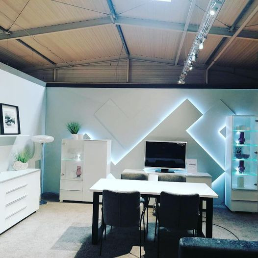 Nowoczesny salon z białymi meblami, stołem z krzesłami i podświetlaną ścianą w geometryczne wzory.