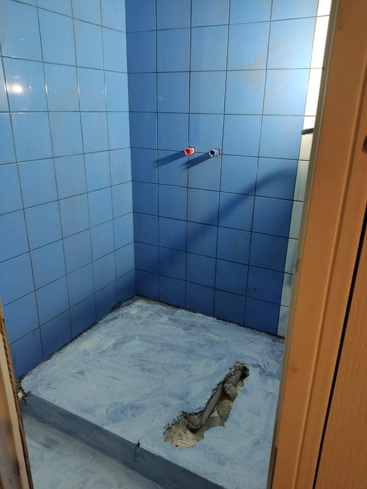 Niedokończona kabina prysznicowa z niebieskimi płytkami, podłoga pokryta warstwą hydroizolacji, widoczne wystające rury instalacji wodnej.