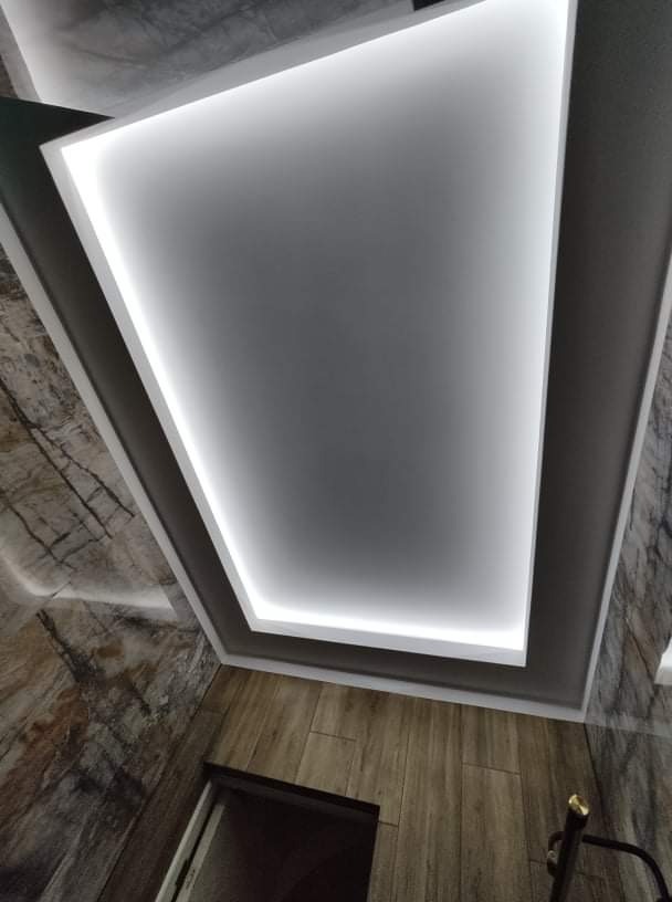 Nowoczesny sufit podwieszany z oświetleniem LED, widok z dołu, z fragmentem ściany imitującej drewno i marmur.