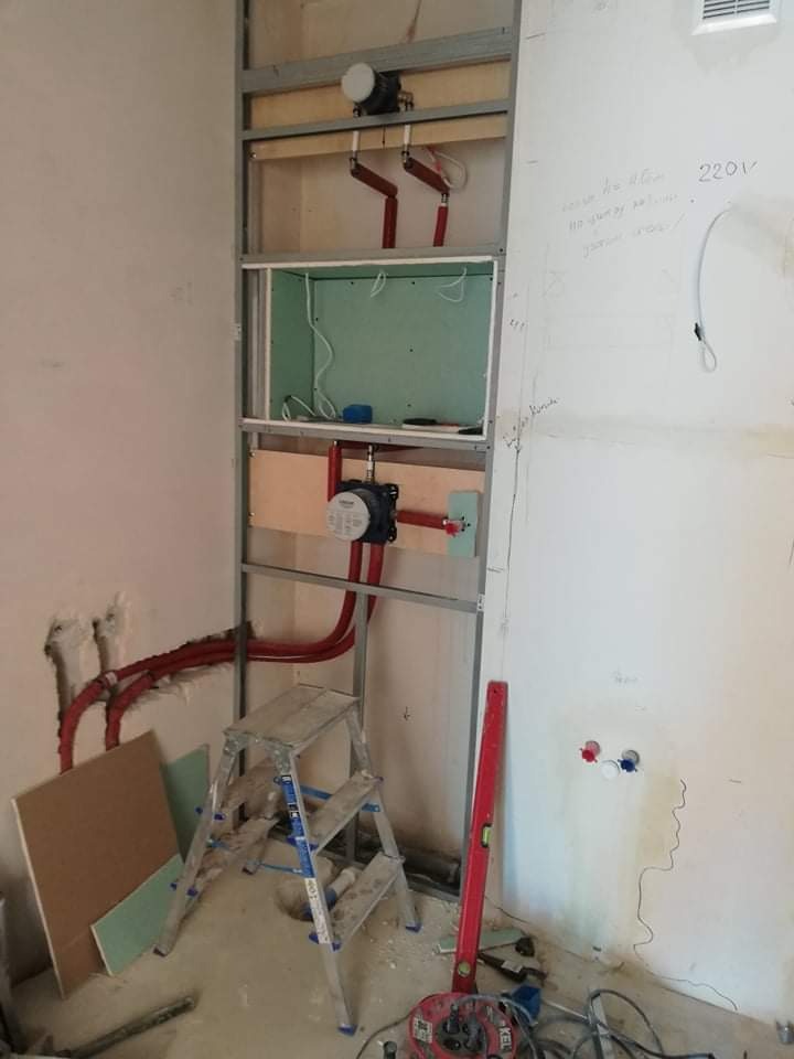 Stelaż pod zabudowę w łazience w trakcie montażu, widoczne rury instalacji wodnej, płyta karton-gips, poziomica i drabinka.
