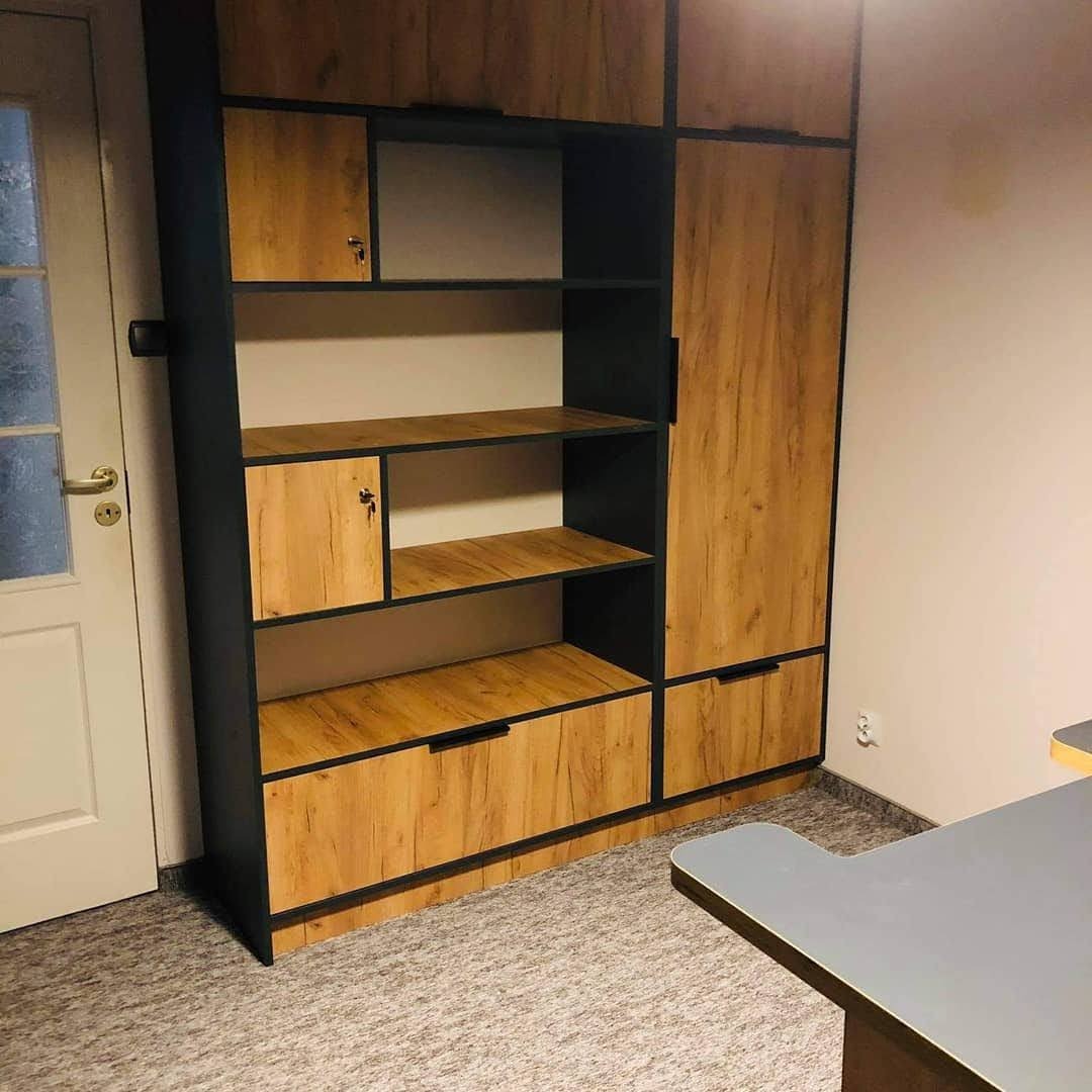 Regał na wymiar z drewnianymi frontami i czarnymi obramowaniami, zamykane szafki na klucz, widok z boku na drzwi i fragment biurka.