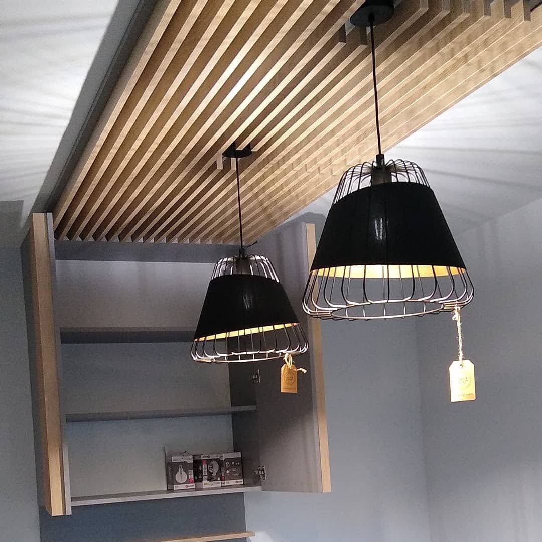 Nowoczesna kuchnia z drewnianym sufitem lamelowym i dwoma czarnymi lampami wiszącymi z metalowymi kloszami, otwarty szary szafka z półkami.