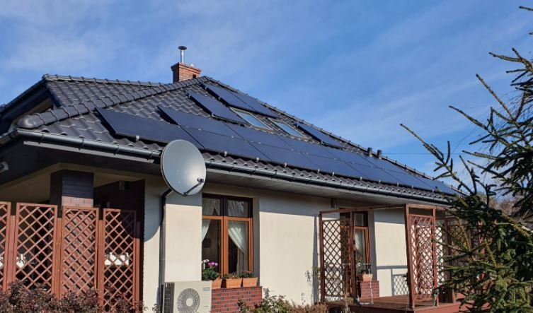 Dom jednorodzinny z panelami słonecznymi na dachu, widoczna antena satelitarna, pompa ciepła na ścianie i fragment ogrodu.