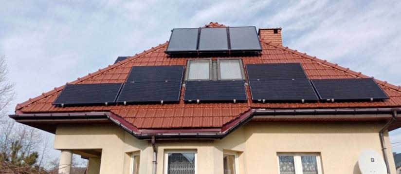 Panele fotowoltaiczne i kolektory słoneczne zamontowane na dachu domu z czerwoną dachówką, widok z dołu.