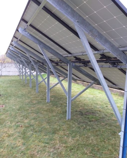 Montaż paneli słonecznych widziany od spodu, z widocznymi metalowymi konstrukcjami wsporczymi na trawiastym terenie.