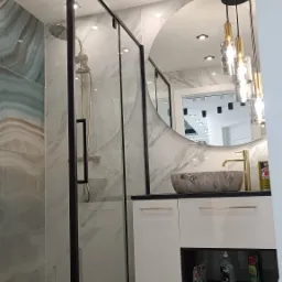 Nowoczesna łazienka z kabiną prysznicową typu walk-in z czarnymi profilami, okrągłym lustrem z dekoracyjnymi lampami wiszącymi i marmurową umywalką nablatową.