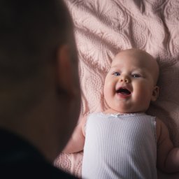 Mateusz Pudło - Uśmiechnięte niemowlę leżące na różowej pikowanej kołderce, skierowane twarzą do osoby poza kadrem po lewej stronie.
